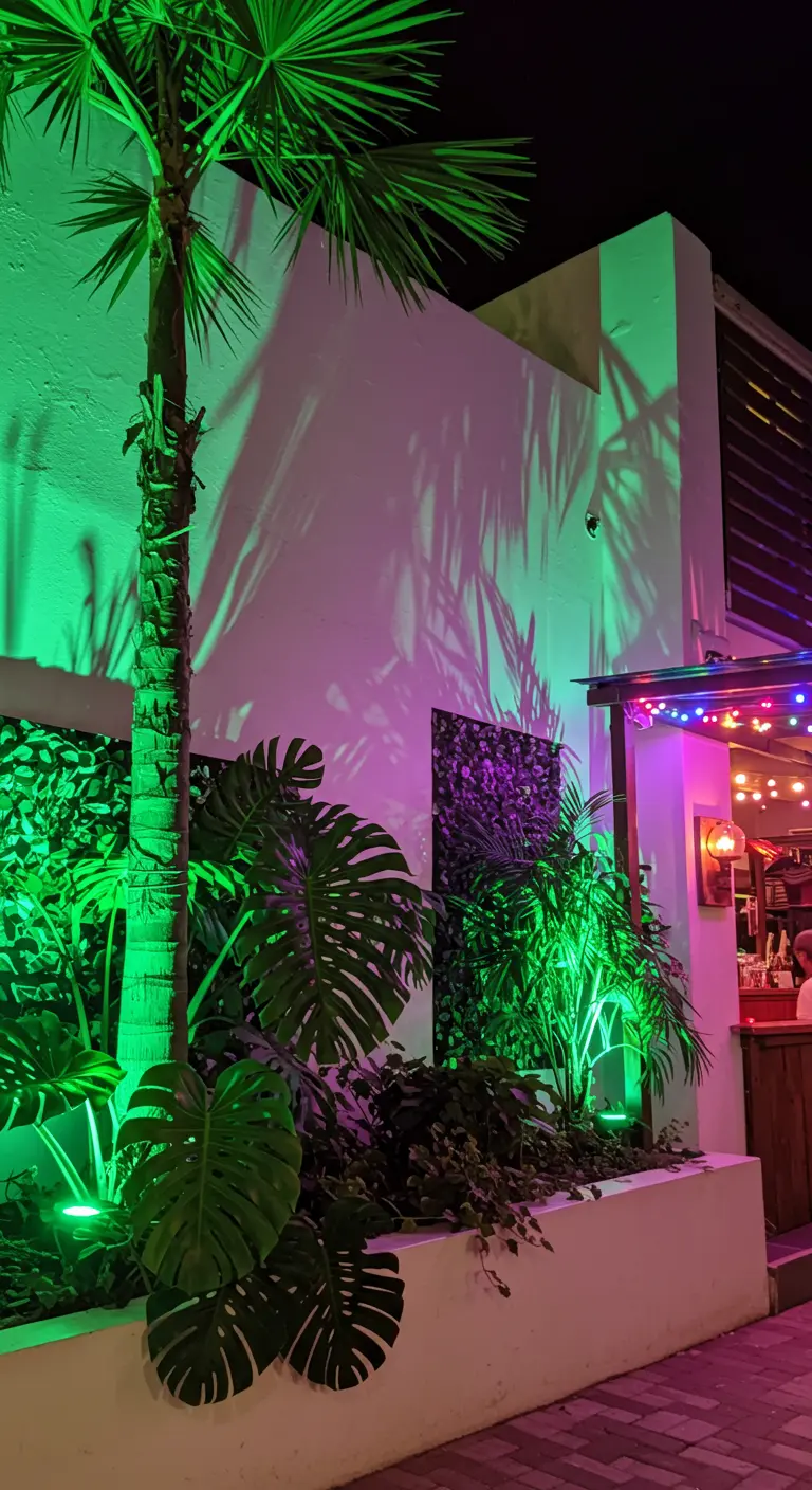 Bâtiment moderne avec palmiers, éclairé par des projecteurs LED colorés et vifs.