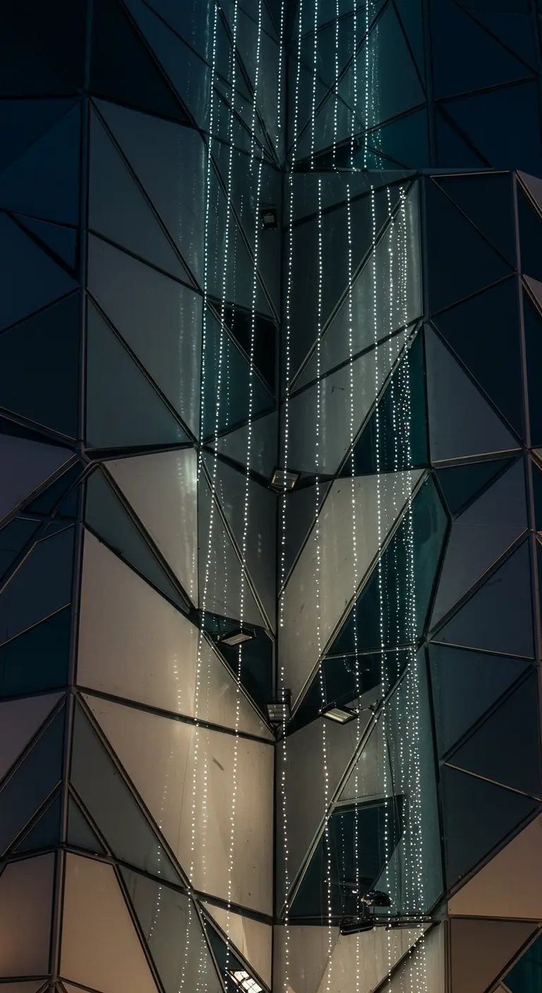 Bâtiment moderne en verre avec des guirlandes lumineuses verticales créant une cascade.