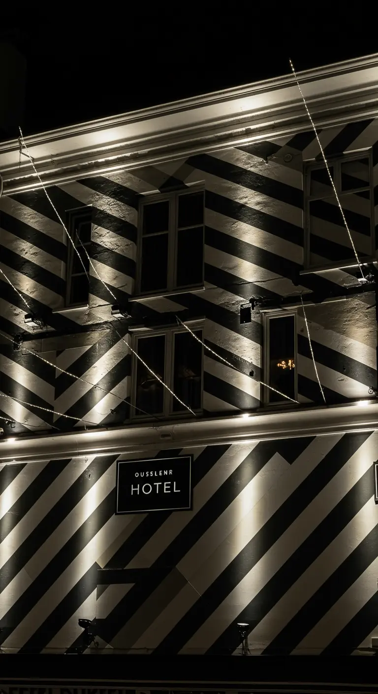 Façade rayée noire et blanche d'hôtel, avec projecteurs et guirlandes diagonales.