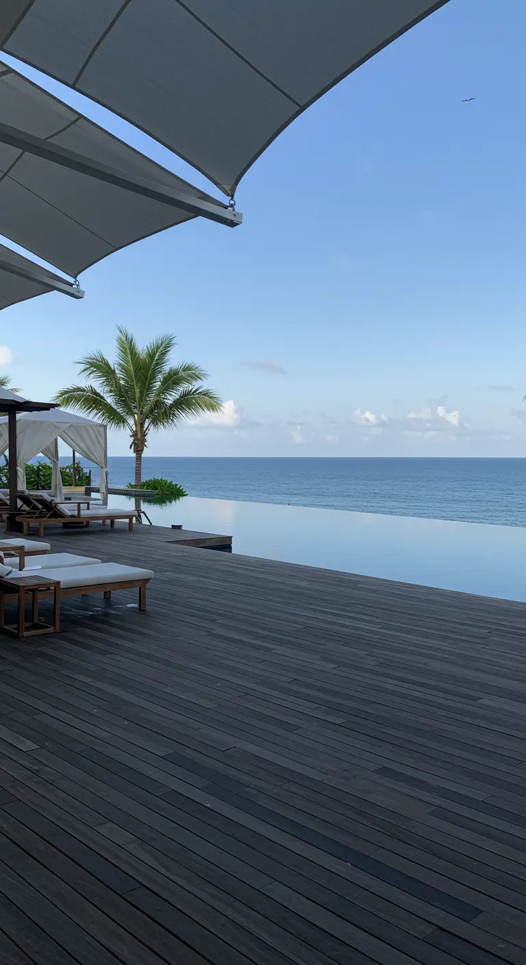 Deck en bois foncé et piscine à débordement donnant sur l'océan, avec des transats modernes.
