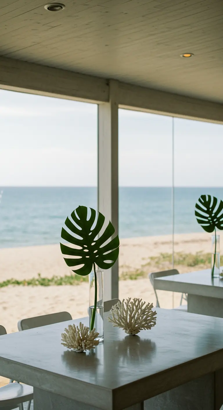 Une seule feuille de Monstera dans un vase sur une table en béton face à la mer.