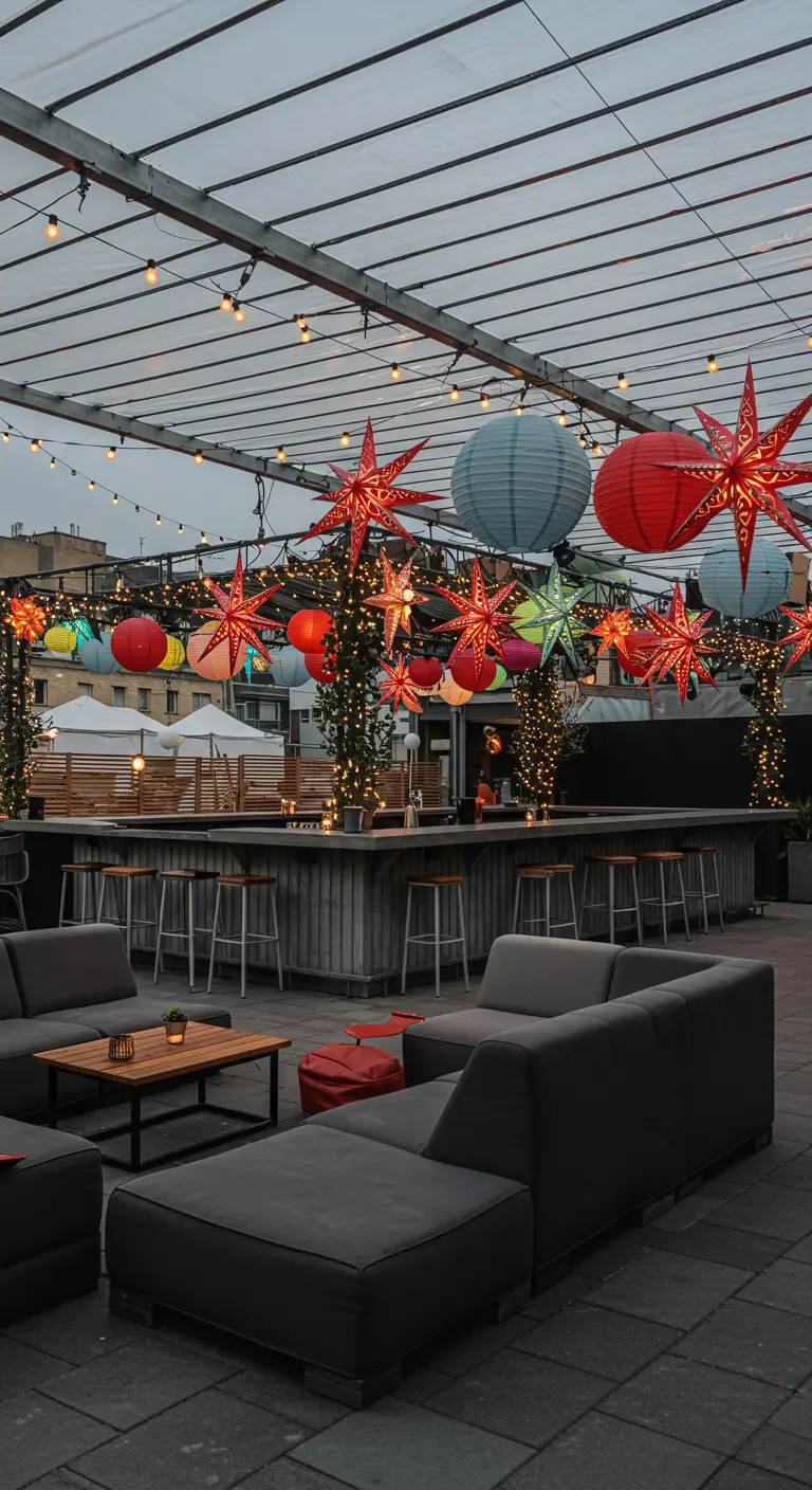 Rooftop bar extérieur avec canapés gris, décoré de lampions colorés et d'étoiles lumineuses rouges et vertes.